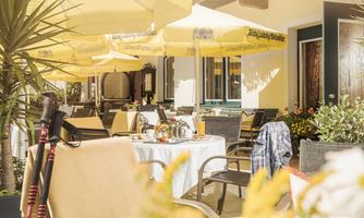 A cozy outdoor area of a restaurant with sun umbrellas and stylish table decorations. Blooming plants and an inviting atmosphere invite you to linger.