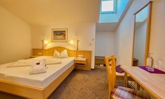 A cozy bedroom with a double bed and a bright atmosphere. The room has a desk and a large mirror.