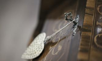 A decorative door handle on an artistically adorned wooden piece of furniture. It is made of delicate metal and is connected by a cord.