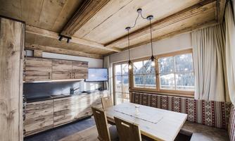 A bright kitchen with a wooden dining area. Large windows offer a view of the surroundings.