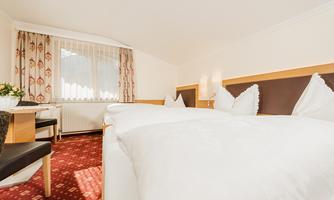 A bright and cozy room with two beds and elegant furnishings. Large windows provide plenty of daylight and an inviting atmosphere.