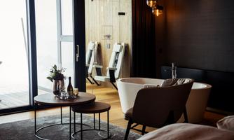 An elegant room with a modern bathroom and a freestanding bathtub. There is a cozy coffee table and a beautiful view through the large windows.
