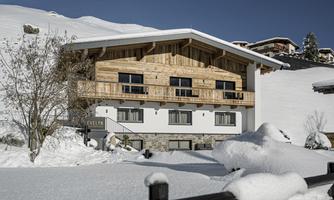 A cozy chalet in the snow with wooden cladding and balconies. The surroundings are wintry and very quiet.