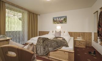 A cozy bedroom with a double bed and wooden furniture. The large windows allow plenty of daylight in and offer a view of the surroundings.