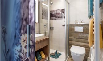 A modern bathroom with a shower, sink, and wooden elements. Towels in various colors are neatly placed on the floor.