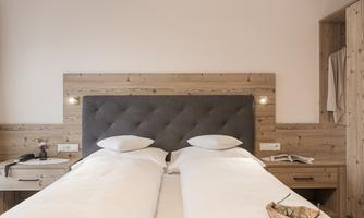 A modern bedroom with two separate beds and a wall clad in wood. There are night lights and a small table with a flower.