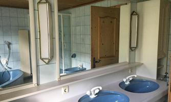 A bathroom with two blue sinks and a large mirror. The walls are tiled and a wooden door is visible.