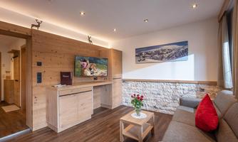 A cozy living room with modern wooden furniture. A comfy couch, a table with flowers, and a flat-screen TV on the wall.