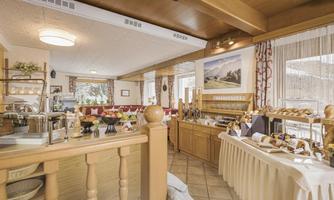 An inviting breakfast room with wooden decor and cozy seating. On a table, various rolls and breakfast options are arranged.