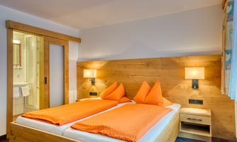 A modern bedroom with two single beds and orange cushions. The walls are made of wood, and there is warm light from the bedside lamps.
