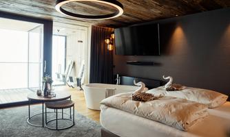 An elegant bedroom with a modern bed and a large window. In the room, there is a bathtub and a round table with chairs.