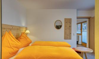 A cozy bedroom with two large orange pillows. The walls are bright and there is a small table as well as a round mirror.