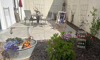 A cozy outdoor area with a table and chairs. Flowers in pots and on the ground create an inviting atmosphere.