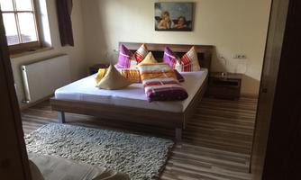A cozy bedroom with a large bed and colorful pillows. The room has a clear, inviting floor and a small rug.