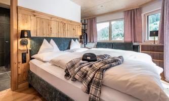 A cozy bedroom with a large bed and wooden paneling. The windows offer a view of a green landscape.