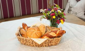 A basket of fresh rolls lies on a table. Next to the basket is a small bouquet of flowers.