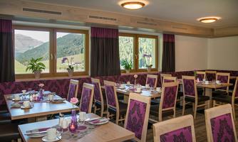 An inviting restaurant with wooden chairs and tables, beautifully set. Large windows offer a view of the surrounding mountains.