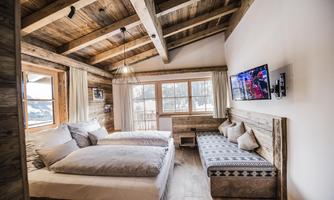 A cozy room with wooden ceilings and two beds.  
Large windows offer a view of nature and a television is mounted on the wall.