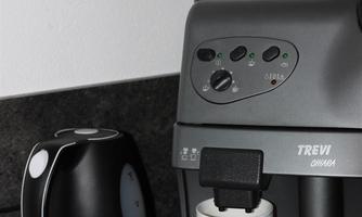 A modern coffee machine stands on the countertop next to a kettle. In front of the machine is a white cup.