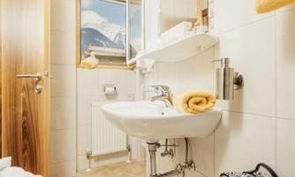 A modern bathroom with a sink and a large mirror. A mountain landscape can be seen through the window.