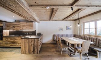 A cozy kitchen in rustic style with wooden furniture and an inviting dining table. Large windows provide plenty of natural light.