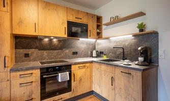 A modern kitchen with wooden cabinets and a serious design. It is equipped with cooking appliances and kitchen utensils.