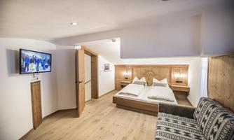 A cozy bedroom with wooden details and a television. There are two beds and a comfortable sofa.