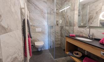 A modern bathroom with a glass shower area and elegant marble. On the countertop, there are towels and care products in stylish design.