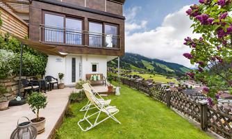 A modern house with a balcony and a beautiful green space. The view of the mountains and the blooming plants creates an inviting atmosphere.