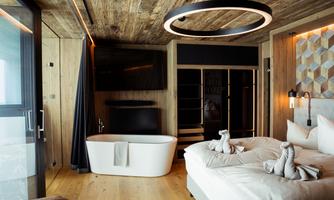 A modern room with wooden decor, a large bed, and a freestanding bathtub. The room is stylishly furnished with a television and elegant lamps.