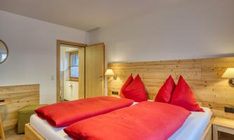 A cozy bedroom with a large double bed and red cushions. The walls are made of light wood, and there is a pleasant, warm atmosphere.
