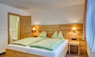 A cozy bedroom with a double bed and green pillows. In the background, there is a bathroom visible through an open door.