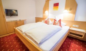 A cozy hotel room with a large bed and red carpet. There is a television on the wall and decorative pillows on the bed.