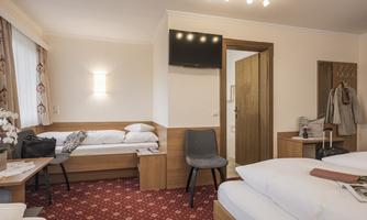 A cozy room with a double bed and a seating area. The room is bright and friendly, with a modern television and carpeted flooring.