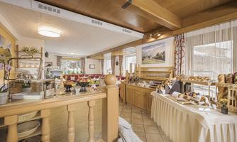 A cozy dining hall with a buffet full of fresh rolls and delicacies. The room is bright and inviting, with wood paneling and tasteful decoration.