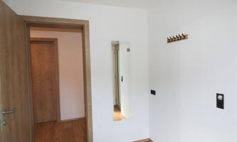 A bright hallway with wooden flooring and white walls. On the wall, there is a mirror and a coat hook.