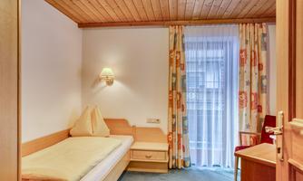 A cozy room with a single bed and bright curtains. The wooden decor and the windows create an inviting atmosphere.