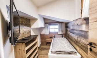 A modern room with wooden walls and a single bed. A television and a window with curtains are also available.