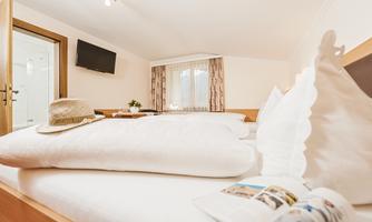 A cozy room with a large bed and a TV on the wall. On the bed lies a hat and a brochure.