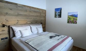 A modern bedroom with a comfortable bed and wooden walls. Two pictures of landscapes hang on the wall.