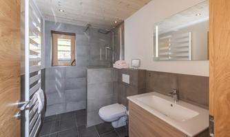 A modern bathroom with a shower and a sink. The walls are painted in neutral gray tones, and there are wooden details.