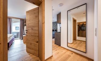 A modern hallway with wood details and a large mirror. An open door and a cozy room behind it can be seen.