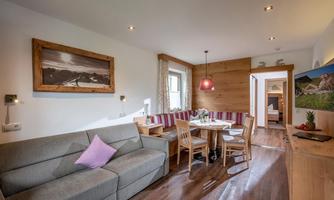A cozy living space with a gray sofa, a dining table, and wood paneling. The atmosphere feels inviting and modern.