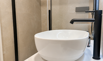 A modern bathroom with a round, white sink and a stylish faucet. In the foreground are two brown cups.