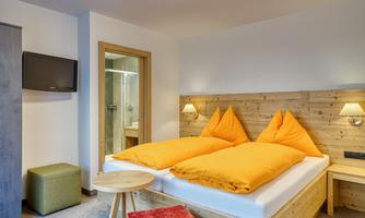 A cozy bedroom with a large double bed and orange pillows. The room features a television and modern bathroom facilities.