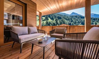A cozy terrace with modern furniture and a view of a forest and mountains. The space is designed with natural wood and offers a relaxed atmosphere.