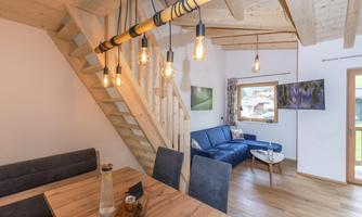 A modern living room with a blue couch and a wooden dining area. The open staircase and warm wood details create an inviting atmosphere.
