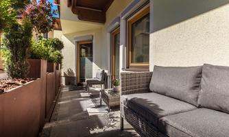 A cozy terrace with modern furniture and plants. The light falls beautifully on the wall and the windows.