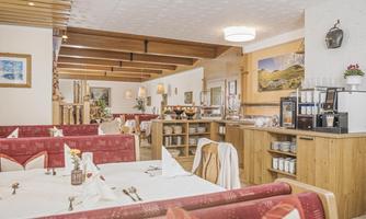 A cozy restaurant with red benches and tables. On one side, there is a buffet area with various foods and drinks.