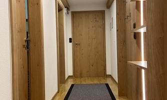 A bright hallway with wooden paneling and a carpet mat. On the wall are shelves with subtle lighting.